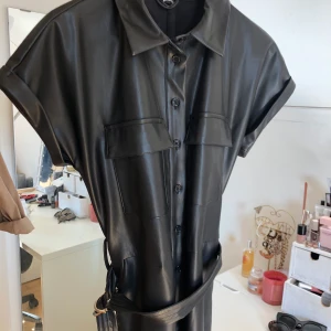 Faux läderjumpsuit från Gina Tricot  - En jumpsuit i läderimitation från Gina Tricot med korta armar och långa ben. Den har en liten reva precis under där skärpet sitter vilket inte syns när man har på sig den (men därav lågt pris). Annars i bra skick! Använd ca 4 gånger. Nypris : 799kr. 