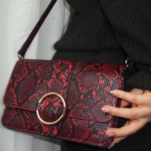 Fake ormskins väska - Röd sidoväska i ormmönster. Guld detaljer med ett långt axelband. Går att användas till både glutch samt axelväska. Aldrig använd då jag tyvärr inte hittar tillfälle för denna fräna väska🤩