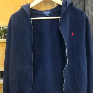 Ralph Lauren huvtröja  - Jättefin trendig Ralph Lauren huvtröja. Den har ett liten hål på baksidan men syns knappt och går säkert lätt att laga. Det finns även en liten mörk fläck längs med dragkedjan men väldigt otydlig, går nog att tvätta bort. Skick 7/10