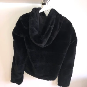Svart Pälsjacka (fake) - Svart fluffig supersnygg och mysig pälsjacka (fake) med stor mysig luva och fickor utan dragkedja. Hällan att hänga upp jackan med har gått av på ena sidan, men går fortfarande att hänga upp den med luvan eller på en galge :) 