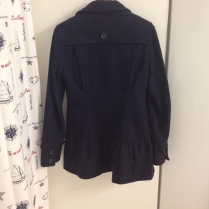 Söt UllKappa med volang och sydda detaljer fram och bak. Marinblå och Mörkrosa inuti. - Söt UllKappa med volang och sydda detaljer fram och bak. Marinblå och Mörkrosa inuti.