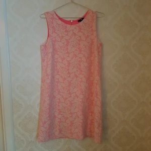  - Äldre klänning från HM i 60-talsstil. Jättefint skick. Passar även M då det är en rak modell. Undertyget är rosa med vit spets utanpå. Dragkedja i nacken. Frakt ingår! 