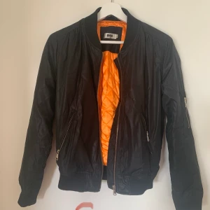 Bomberjacka  - Svart bomberjacka med orange tyg på insidan. 