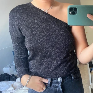 One shoulder topp - Glittrig svart one shoulder topp. Perfekt för partaj nu när det börjar bli mörkare. Storlek 38, i väldigt bra skick.