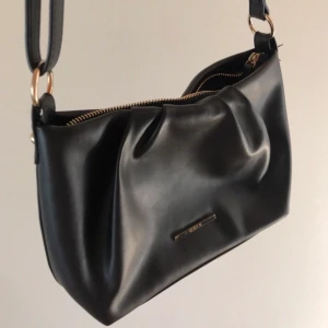 Handväska i fakeskinn - Denna superfina handväska har justerbara axelband, ett guldigt märke och fack inuti. Kostar 60kr exklusive frakt