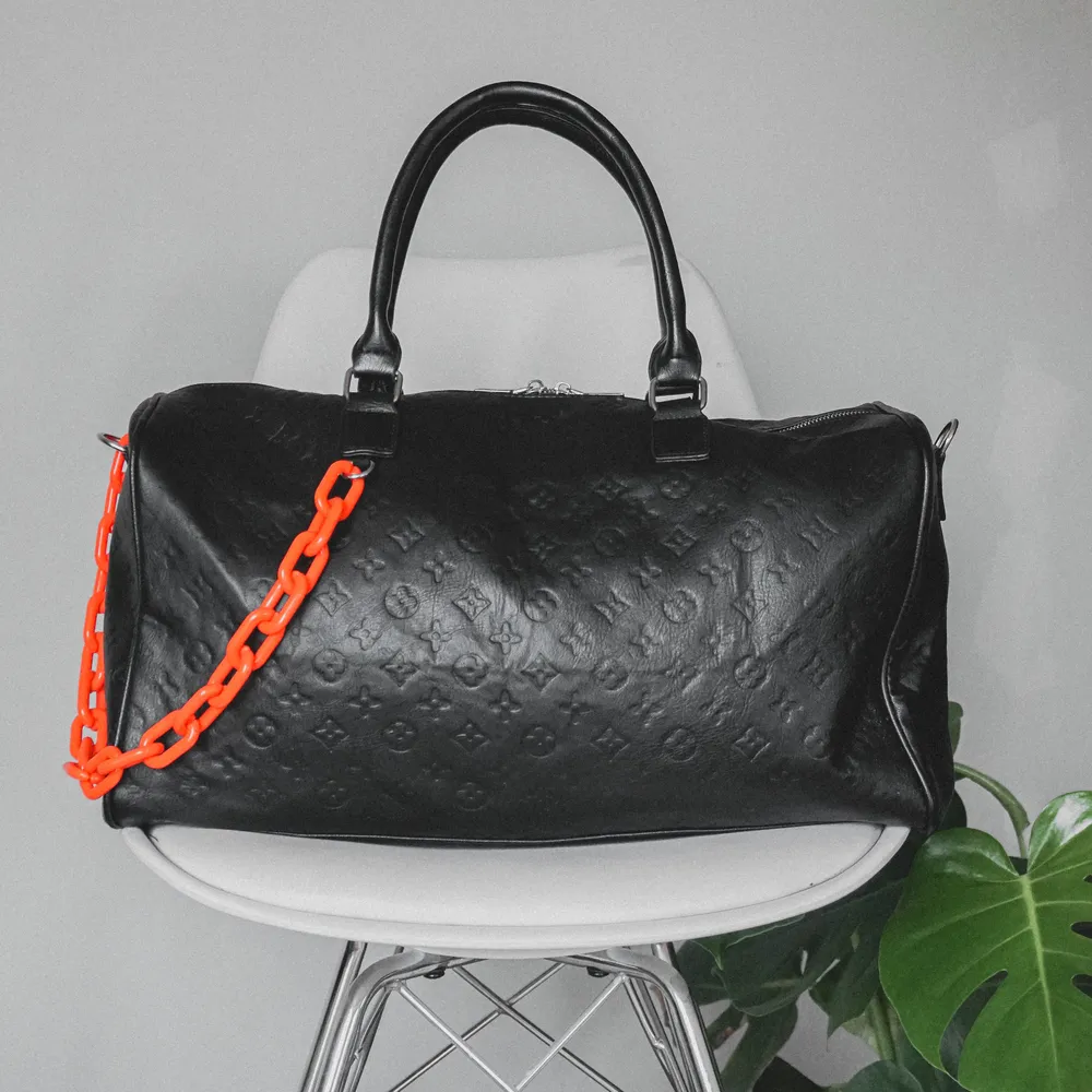 Snygg, stilren väska inspirerad utav Louis Vuitton. Svart med orange plastkedja. Rymmer förvånansvärt mycket, kan användas som ”weekend”-bag. Aldrig använd och har, tyvärr, bara legat i garderoben.. Väskor.