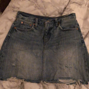 Levis jeanskjol - En snygg och stilren jeanskjol från Levis med små inte allt för diskreta slitningar. Strl 25 motsvarar xs/s vilket var vad jag pendlade mellan när jag köpte kjolen. Säljes pga att den är för liten, köptes originalt för 700kr. Perfekt inför sommaren (!!!)