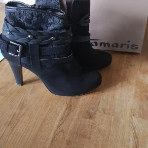 Stövlett Tamaris  - Svart högklackad stövlett i mocka med spänne, detaljer och remmar. 10 cm klack, använd 1 gång.