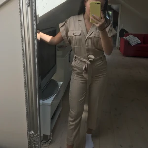 Beige jumpsuit - Supersnygg byxdress från H&M. Köpte förra sommaren men den har inte kommit till användning, så den är helt oanvänd med prislapp kvar. Nypris 400, frakt tillkommer