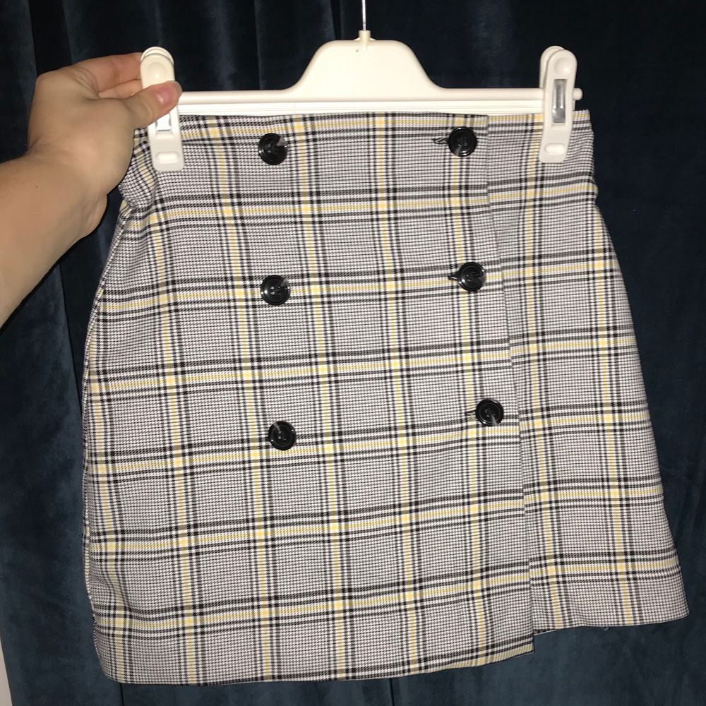 Grå kort kjol med gult schack mönster. Älskar denna kjol då jag får Legally blond vibes. Tyvärr passar den inte längre så vill ge någon annan få känna sig som en boss! Det är en wrap kjol så man stänger kjolen med knapparna. Kjolen är i bra skick. Den är i storlek 34 / xs.. Kjolar.