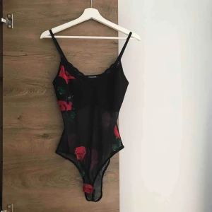  - Tight stringbody! Svart med ros-tryck, transparent tyg över mage och rygg med knappar i grenen. Använd fåtal gånger, bra skick! Dock en av spännena på axelbanden som är lite trasig, den fungerar men är lite lös. 