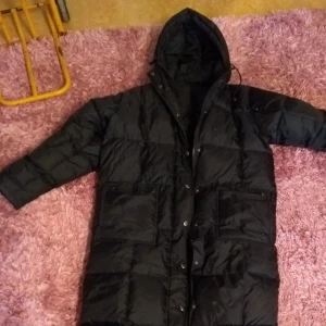  - Lång svart täckjacka som räcker med till vaderna. I begagnat fint skick!