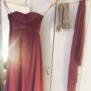  - Superfin balklänning i mörkrosa som övergår till ljusrosa! Använd endast en gång, storlek M men rymlig över byst. Köptes för 2000 kr i butik. Champagnefärgade handskar och sjal i samma tyg ingår i pris. Frakt står köparen för! 