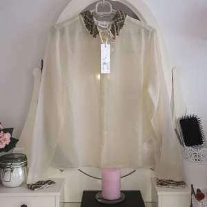  - Ursnygg lyxig skjorta med fina detaljer. Genomskinlig créme vit/beige färg. Passar en small och större x-small. Aldrig använd, med lappar fortfarande. Finns i Stockholm. Fraktas mot en extra slant och betalning sker via swish. :)