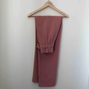  - Rosa högmidjade kostymbyxor med knytning i midjan. Avända 2 gånger så i princip nyskick<3 Kan mötas upp längst roslagsbanan eller i stockholm, annars står köparen för frakt.