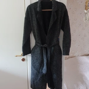  - Längre och tunnare kappa i melerad polyester och ull. Använt skick. 