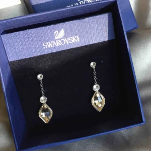  - Örhängen med Swarovski kristaller från More to Adore by Swarovski. Den nedre kristallen skiftar i rosa och de övre mindre är helt neutrala. Silver. Använda ett fåtal gånger.