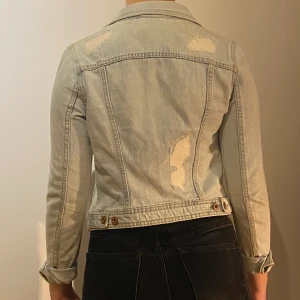 Jeansjacka  - Jeansjacka i ljusblått tyg. Med ”slitningar” här och där. Jättefin men liten i storleken, skulle säga xs. 