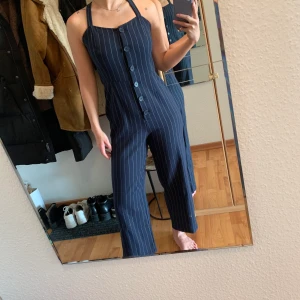 Monki kritsträcksrandig jumpsuit  - En väldigt skön och figursydd marinblå byxdress/jumpsuit. Benen är vida och banden går att justera, man kan även sätta banden i kryss. Man får absolut plats med att ha nånting snyggt under även! Skick: 4 av 5. Hel och ren! 