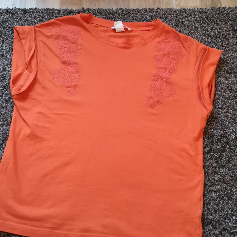 Orange t-shirt med något liknande blom/kurbits mönster på framsidan. . T-shirts.