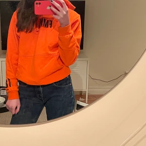 Orange hoodie - Hoodien är från kollektionen mellan Lisa Anckarman & madlady. Den är i bra skick! Passar perfekt till ett par låg midjadejeans. De står ”feminist” på framsidan. Och på armen ”18” och på baksidan ”EMPOWER”.