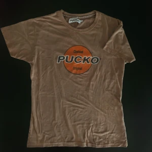 retro PUCKO t-shirt beige - Asball t-shirt från PUCKO vintage i beige/brun nyans! Storleken passar en Medium om man vill att den ska sitta tight, för lösare passform skulle jag säga S/xs🍀 (läs min bio innan beställning)