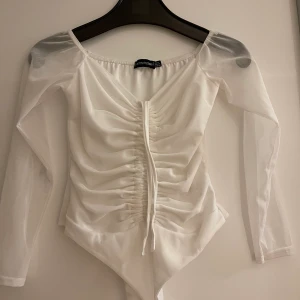 En vit body från Pretty little thing. - Vit body med drag på framsidan med genomskilninga armar.