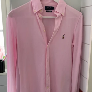Polo Ralph Lauren Skjorta - En rosa skjorta i ett annorlunda material, jättebekväm! är för liten för mig tyvärr! använd endast en gång! frakt ingår ej i priset! Pris kan diskuteras!