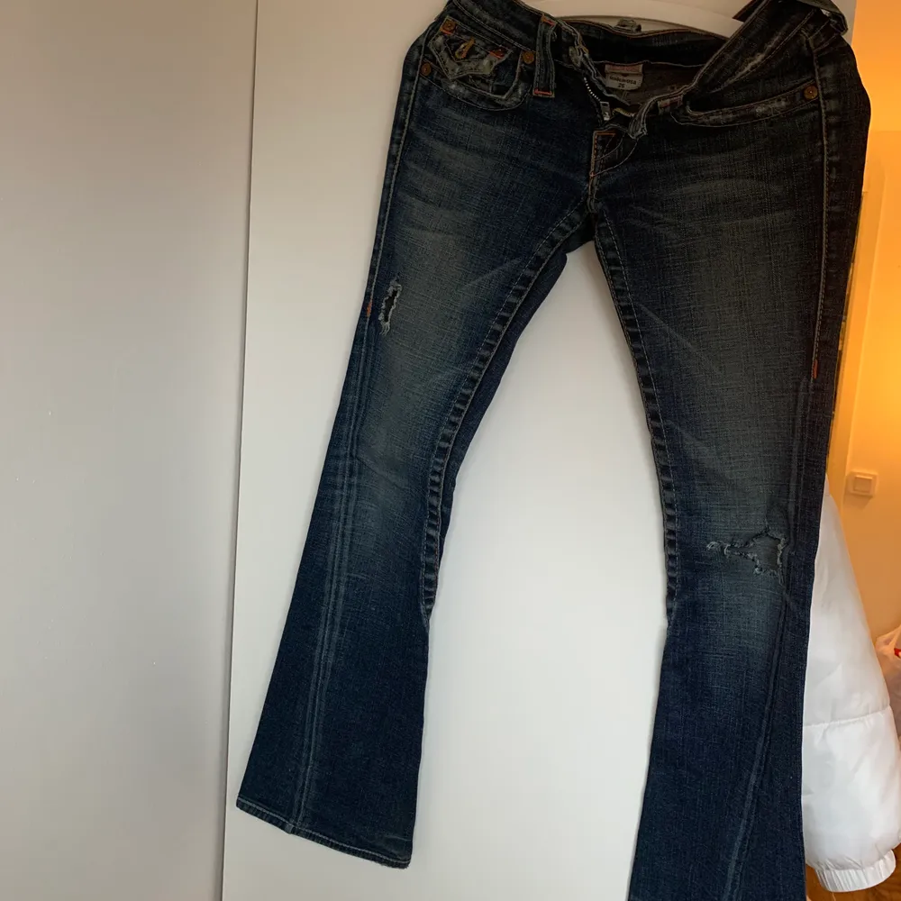 Lågmidjade mörkblåa jeans från märket true religion. Tyvärr alldeles för små och korta för mig som är 165, säljs pga det. Har två hål, slitningar i vardera ben.. Jeans & Byxor.