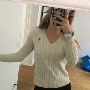 Kabelstickad Tröja Ralph Lauren, Beige XS - V-ringad, Beige Kabelstickad tröja från Ralph Lauren i storlek XS. Fint skick förutom en liten fläck längst ned på tröjan (se tredje bilden).