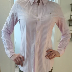Ralph Lauren skjorta  - Ljusrosa- och vitrandig skjorta från Ralph Lauren med custom fit. Knappt anvönd, säljer för att jag inte passar i rosa. Frakt ingår i priset! 
