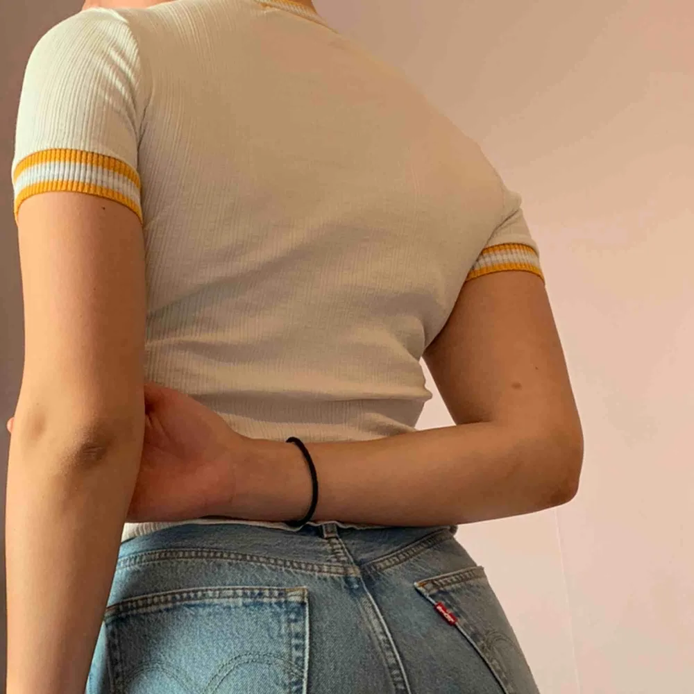 Vit t-shirt med gul/orangea detaljer Passar till allt ifrån ett par Ripped jeans till en gullig mini-kjol🤍💛🧡. T-shirts.