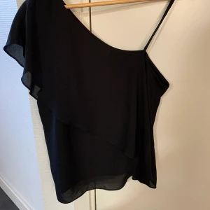 One Shoulder - Svart OneShoulder blus, i bomull. Löst sittande. Str.38.