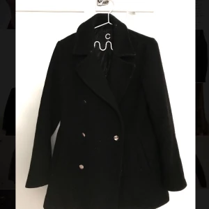  - Svart kappa i ullmix. Fin a-linjeformad modell med knäppning i gulddetaljer. Guldiga knappar vid ärmslutet.   Upphämtning Stockholm innanför tullarna. Fraktar gärna, pris beroende på fraktform. ❄️💫