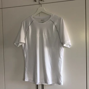 Vit tränings t-shirt - Vit tränings t-shirt i storlek M från Craft. Två gråa sömmar framtill och även ett vitt (craft)tryck.