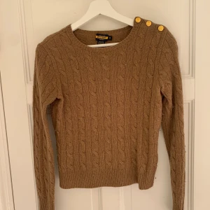 Kabelstickad Ralph lauren tröja  - Kabelstickad tröja från Ralph Lauren med guldknappar på vänstra axeln. Fint skick men lite nopprig Storlek S 