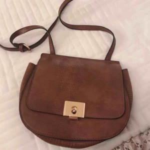  - Brun väska med svarta sömmar, och guldiga detaljer! Den är även justerbar, och går att göra längre/kortare!:)  Kan hämtas i Varberg, annars står köparen för frakten!:)