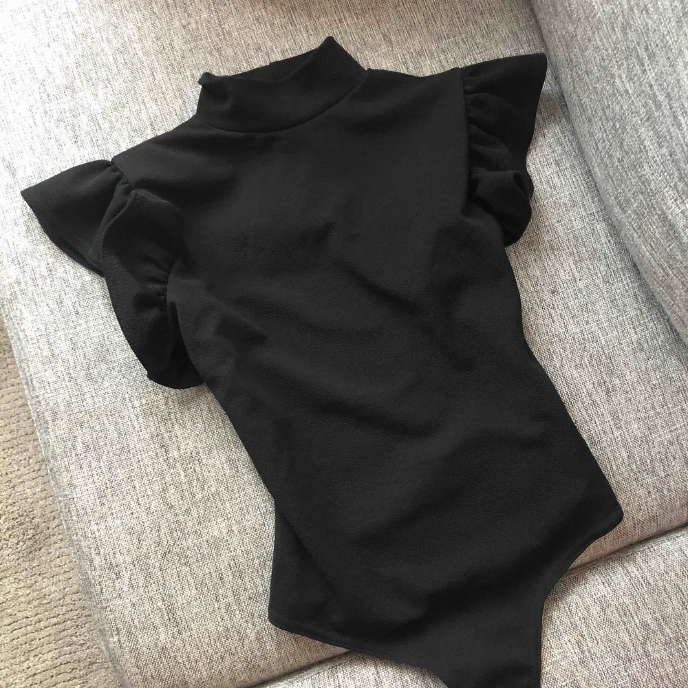 Svart body med volang detaljer runt axlarna och hög krage. Provad 1 gång, aldrig använd.  Etiketten sitter fortfarande kvar.  Butikspris 250:-  95% polyester  5% elastan Frakt ingår. . Toppar.