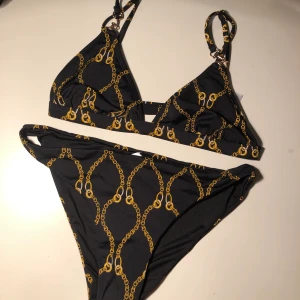 Svart bikini  - Svart bikini med mönster av guldiga kedjor. Köpte inför en utlandsresa och använde en gång, efter det har den ej kommit till användning. Märket är HappyHolly. Toppen är i strl 32/34 men är stor så den passar även 36/38 och underdelen är i 36/38. 