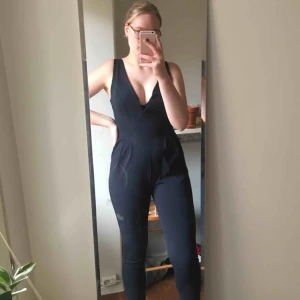  - Mörkblå jumpsuit. Dragkedja i ryggen och fin urringning. Fickor fram. 