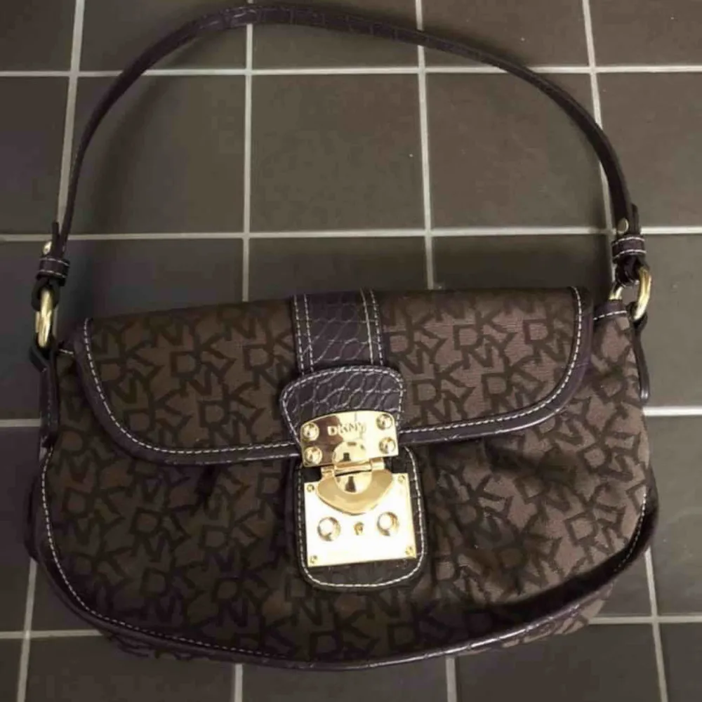 Sjukt fin väska från märket DKNY! Påminner lite om en LV väska i färg och form när han hänger den över axeln. Guld detaljer och skinn detaljer! Kan skicka men då betalar köparen för frakten :) . Väskor.