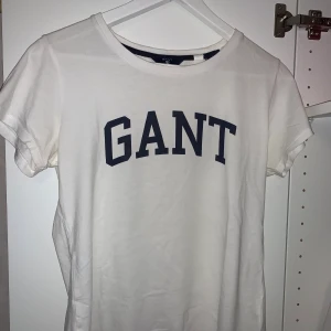 T-shirt från GANT - Vanlig vit t-shirt med marinblått tryck, inte använd speciellt många gånger, har dock några knappt märkbarq färgfläckar, storlek S💞💞