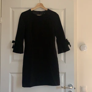 Svart klänning med detaljer  - Supersnygg svart figursydd klänning med detaljer från Mango. Detaljerna sitter på ärmen och är rosetter, det är även en dragkedja bak på ryggen. Storlek XS, säljer för 90kr. 