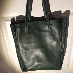  - Grön väska med guldiga dragkedjor som man kan dra ner och upp för att göra väskan rymligare eller mer kompakt. Skick är som nytt. Köpt i Barcelona. Endast ett litet fack på insidan 