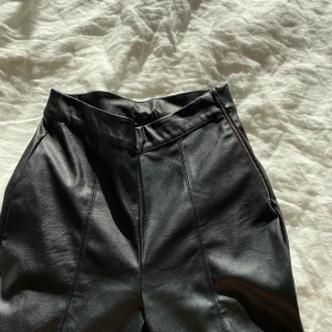 Svart skinnbyxa - Svart skinnbyxa i fejkskinn ifrån Gina Tricot. Korta i modellen och med detalj som längs med benen. 