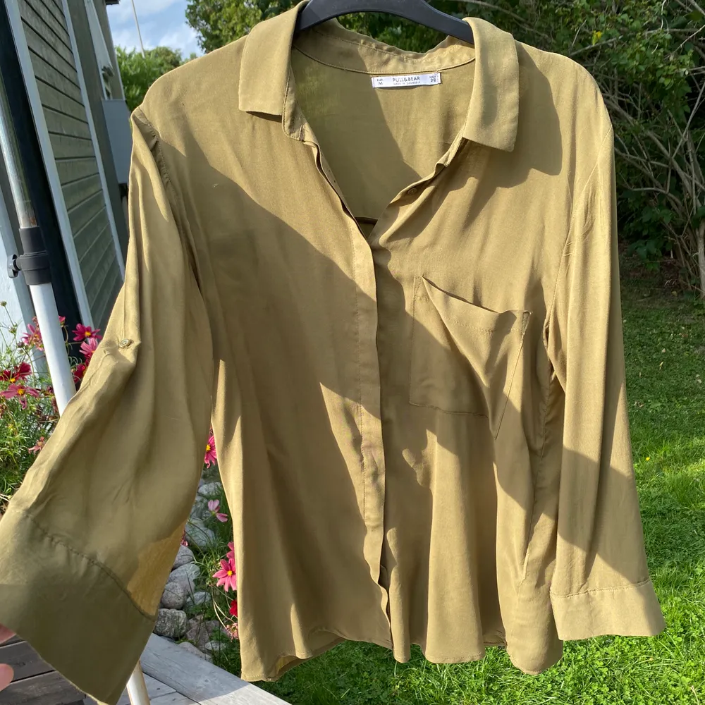 Grön skjorta från Pull & Bear. Ficka på ena sidan och ärmarna går att fästa med en knapp längre upp vid armvecket. Använd cirka 3 gånger. Fraktavgiften står köparen för!. Skjortor.