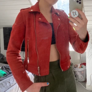 Mocka jacka - En röd jacka av mocka med guldiga detaljer. Sitter snyggt och bekvämt med bra passform. Storlek 36 och sitter lagom tajt/löst. 