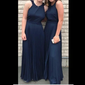 Marinblå balklänning med kryss i ryggen - Superfin blå balklänning från Nelly som har en plisserad kjol nertill och öppen rygg med ett kryss i ryggen av volanger. Liten fläck på framsidan finns, men syns knappt. 150kr exklusive frakt 