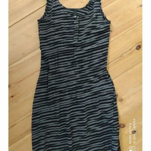 Figurnära HM klänning - Svart/grå tigerrandig. Knäppning i urringningen. Sitter riktigt snyggt på! Djur och rökfritt hem.Frakt tillkommer på 44:- jag samfraktar gärna!
