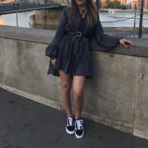 En söt klänning från h&m - En svart långärmad kort klänning  med vita mönster. Jätte fin modell som passar fint med både skärp och utan skärp. Använd endast en gång. 